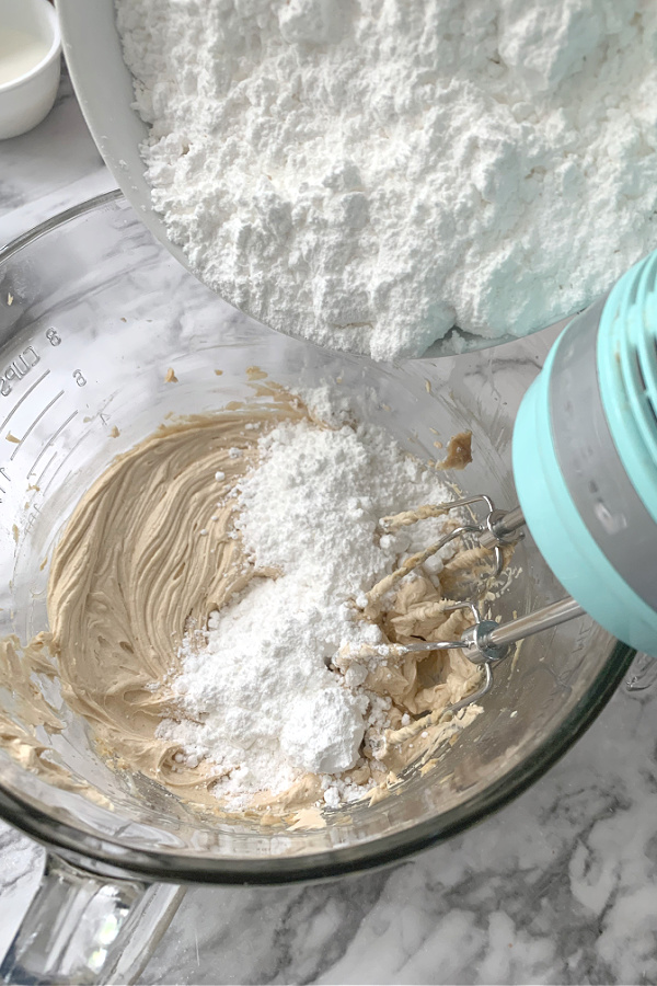 Adding confectioners sugar to the creamed mixture for making Peanut Butter Frosted Brownies recipe.