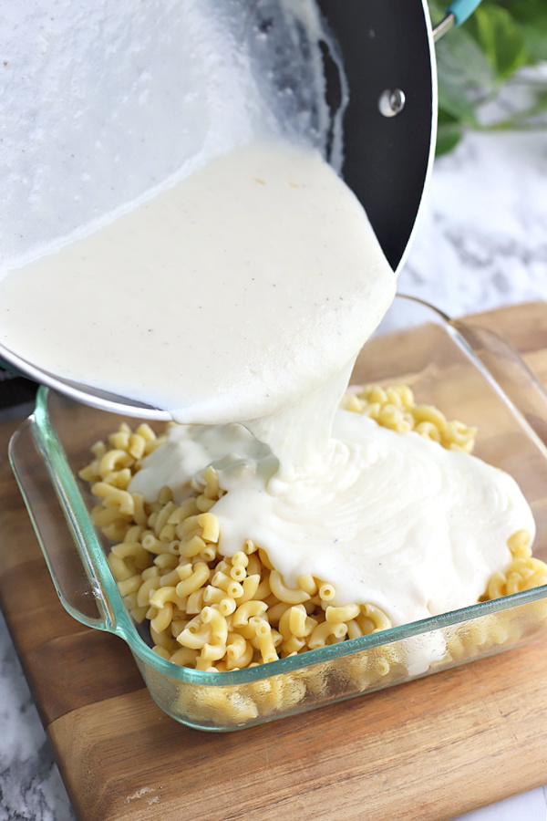 pouring cheddar cheese sauce over elbow macaroni