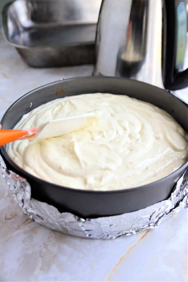 adding the cream cheese batter to the prepared springform pan for lemon curd cheesecake.