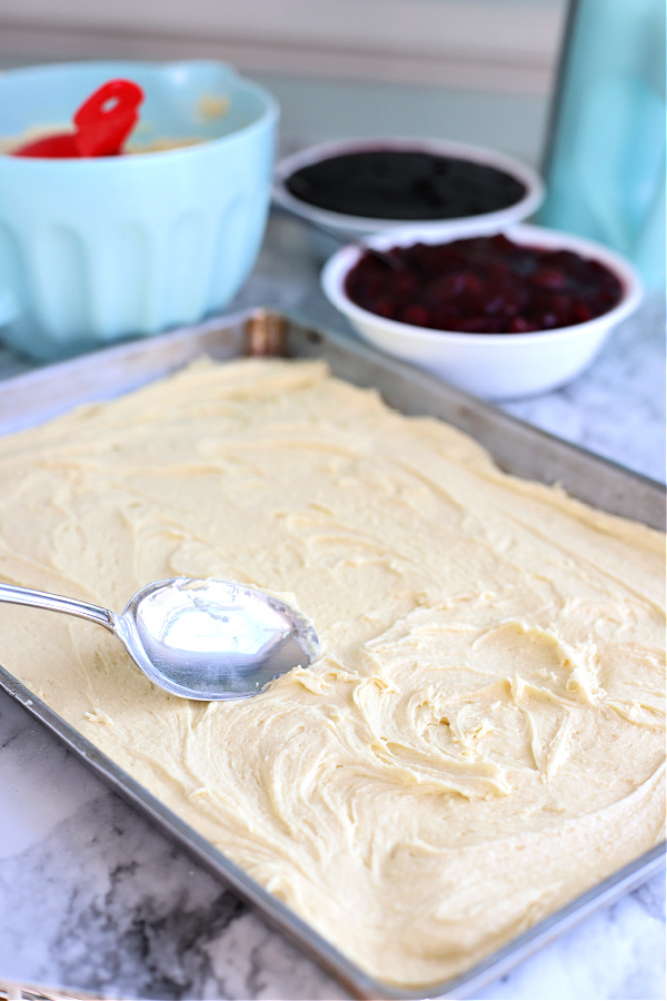 Spooning the batter onto a sheet pan for cherry blueberry fruit bars.