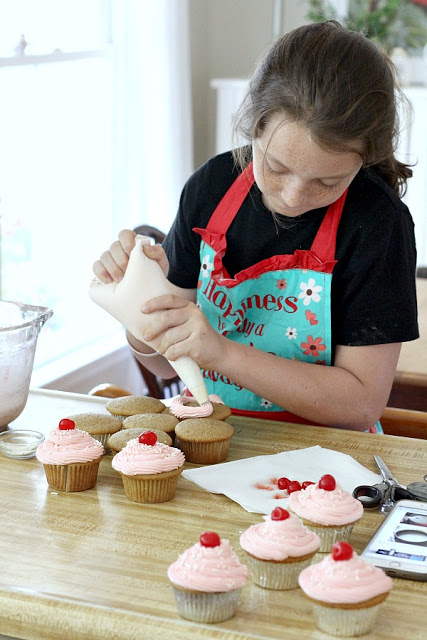 piping cherry frosting onto cupcakes