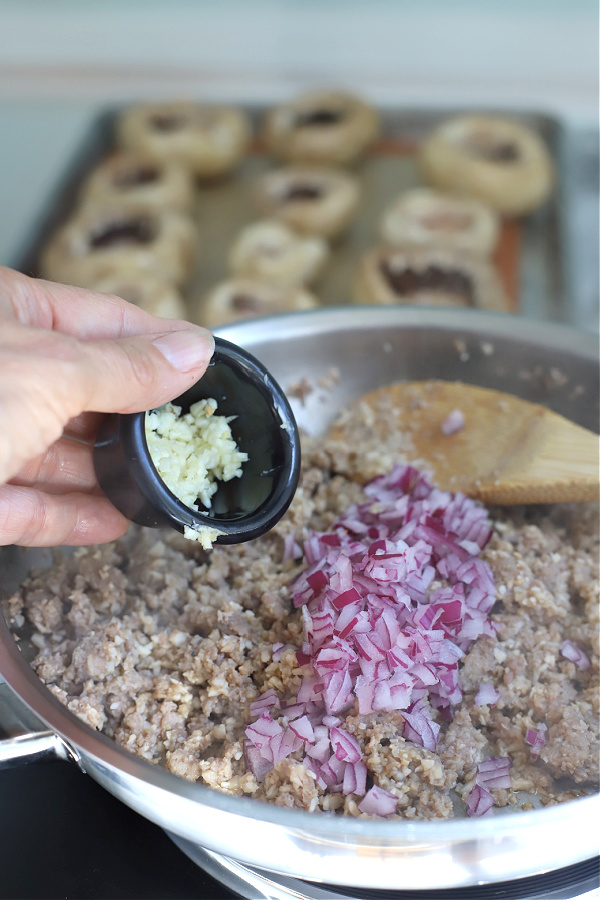 adding garlic and red onion to sausage stuffed mushrooms filling