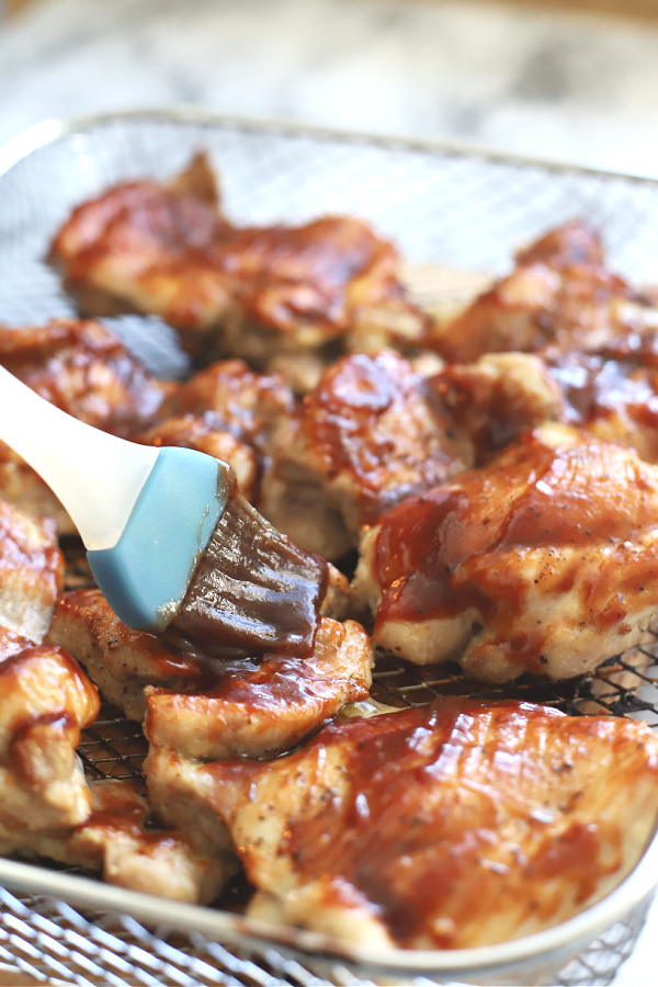 Basting pieces with barbecue sauce for skinless, boneless BBQ chicken thighs in the air fryer.