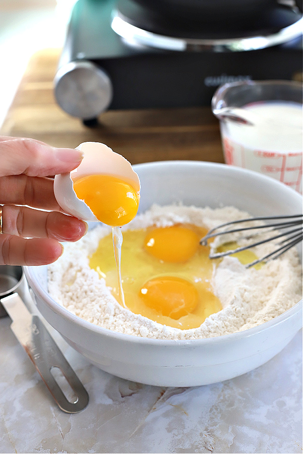 Adding eggs to flour ingredients for manicotti crepes.