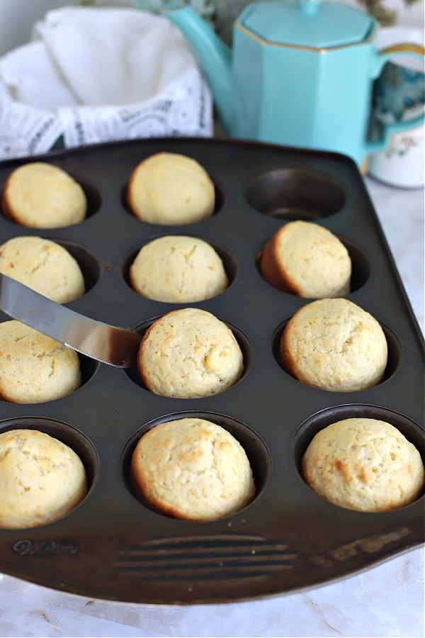 Carefully removing the baked basic muffins from the pan.