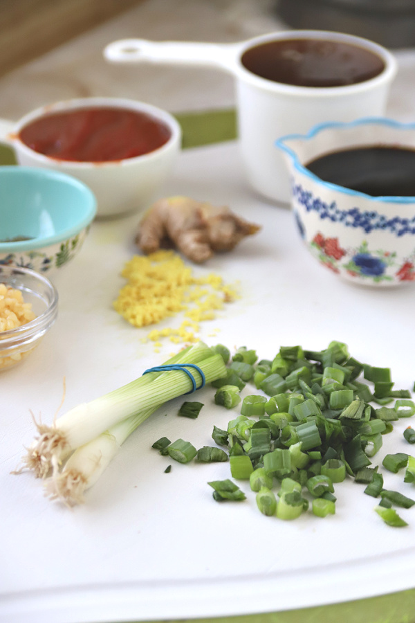 Chopping green onions and grating fresh ginger for honey garlic sticky chicken wings appetizer recipe.