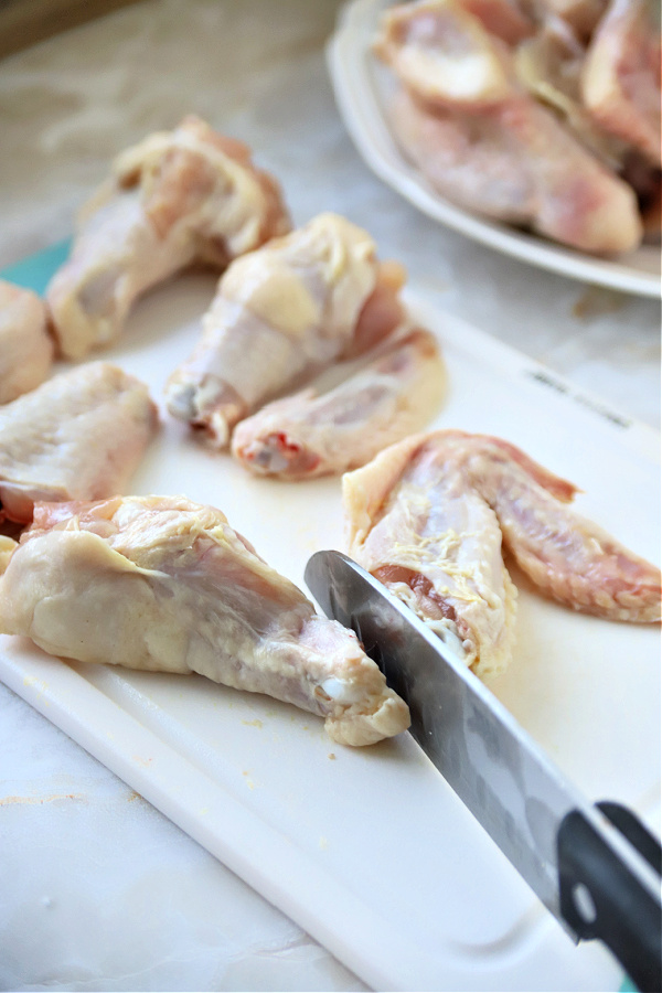 Preparing honey chicken wings recipe by cutting the raw wings segments into pieces.