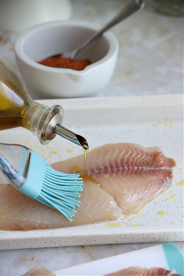 brushing olive oil on fish for baked blackened tilapia