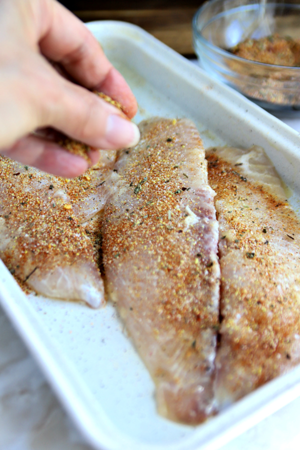 Sprinkling herb and spice mixture onto fish for blackened tilapia.
