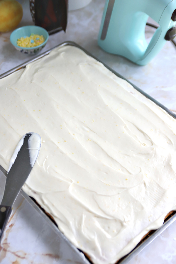 Spreading cream cheese frosting on cooled lemon sheet cake.