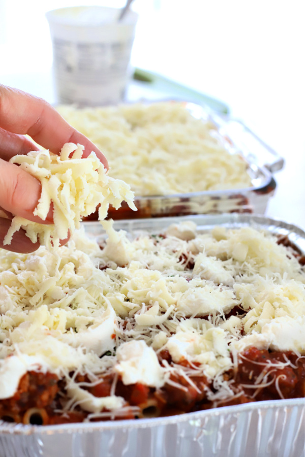 adding mozzarella and parmesan cheese to baked ziti casserole.